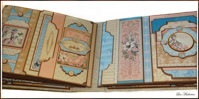 May include: Open scrapbook with multiple pages. The pages feature a mix of light blue, peach, and tan patterned paper. Decorative elements include floral illustrations, framed images of women, and the text "My Sweet Princess".