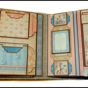 May include: Open scrapbook with multiple pages. The pages feature a vintage design with floral and crown patterns in shades of blue, pink, and beige. One page has the text "A woman can be overdressed if she is not elegant."