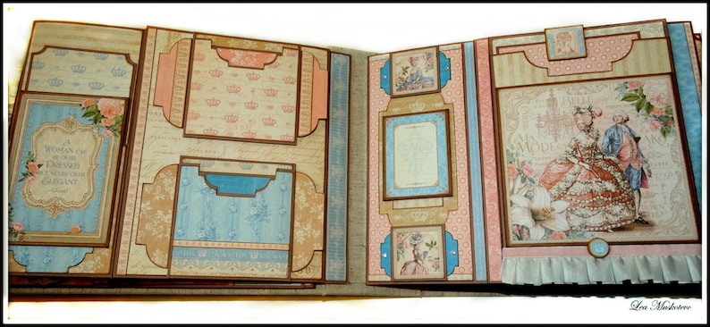May include: Open scrapbook with multiple pages. The pages feature a vintage design with floral and crown patterns in shades of blue, pink, and beige. One page has the text "A woman can be overdressed if she is not elegant."