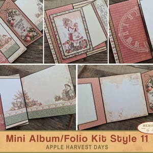 May include: A multi-panel mini album folio kit featuring an apple harvest theme with pink, green, and cream paper. The design includes illustrations of a child with apples, a clock face, and a tag labeled Homemade Apple Jam. The kit has blank spaces.