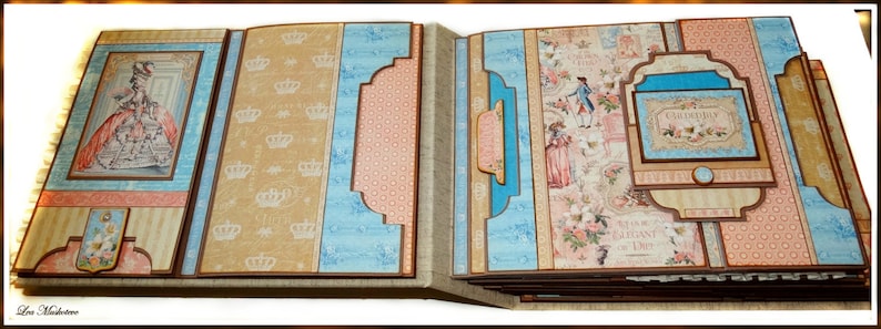May include: A handmade scrapbook with a vintage theme. The pages feature illustrations of people in period clothing, crowns, and floral patterns. The color palette includes shades of blue, peach, and tan, with brown borders.