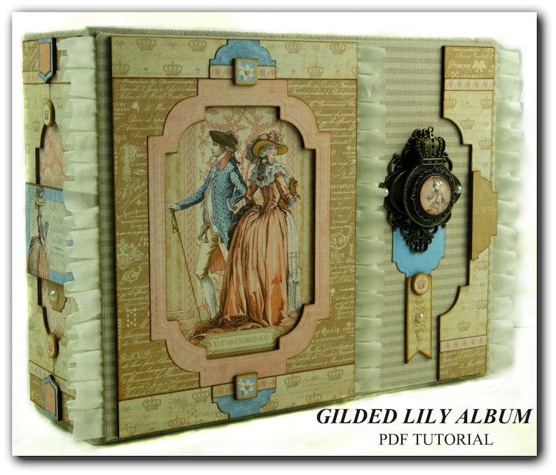 May include: A decorative scrapbook album with a vintage aesthetic. The cover features a framed illustration of a couple in period clothing. The album is embellished with decorative elements, including a metal clasp and ribbon accents. The text "GILDED LILY ALBUM PDF TUTORIAL" is visible.