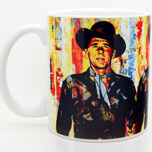 Pu&ograve; includere: Tazza da caff&egrave; in ceramica bianca con un'immagine colorata di un uomo con un cappello da cowboy e una camicia nera. Lo sfondo &egrave; un design astratto colorato.