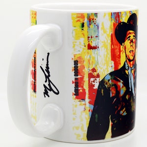Pu&ograve; includere: Tazza in ceramica bianca con un design astratto colorato che presenta un uomo con un cappello da cowboy. La tazza ha una firma nera e il testo "Edition # 00005".
