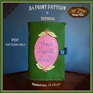 May include: A green felt book cover with a pink oval applique that says "The Secret Book". The cover has a blue button and a green felt strap. The finished size is 14 inches by 9 inches.