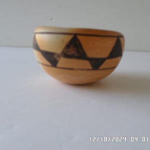 May include: A small, round, ceramic bowl with a geometric pattern of black triangles on a light brown background.