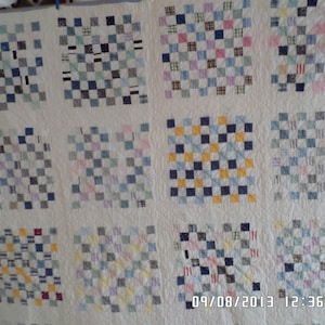 May include: A handmade quilt with a grid pattern of small squares in various colors, including blue, yellow, pink, and gray, on a cream background. The quilt is likely made of cotton or a similar fabric. The date 09/08/2013 12:36 PM is visible.