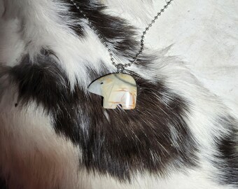 May include: A silver chain necklace with a white and brown stone bear pendant. The bear is carved in a simple, stylized design.