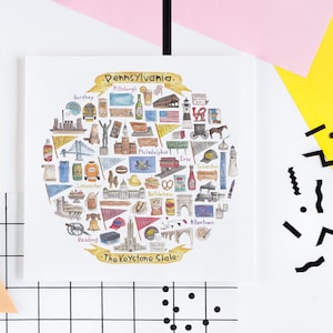 Puede incluir: Una ilustración de acuarela de un mapa en forma de corazón de Pensilvania con varios iconos que representan diferentes ciudades y monumentos. El texto "Pennsylvania" y "The Keystone State" están incluidos en la ilustración.