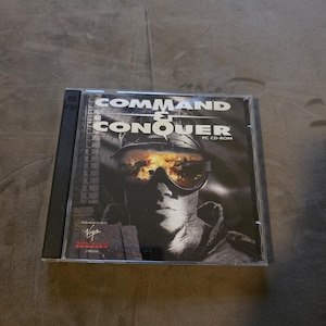 May include: A Command & Conquer PC CD-ROM game in a clear plastic case. The cover features a black and white image of a person wearing goggles, with the game title in bold white letters.