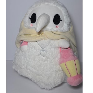 May include: A plush toy in the shape of a plague doctor with a white face, a long white beak, and large black eyes. It wears a cream-colored hood and holds a pink and yellow lantern. A silver heart pendant hangs from its neck.