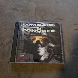 May include: A Command & Conquer PC CD-ROM game in a clear plastic case. The cover features a black and white image of a person wearing goggles with a fiery reflection. The game title is in bold white letters.
