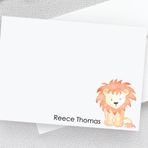 May include: A white card with a watercolor illustration of a cute orange lion with a brown mane. The card has the name "Reece Thomas" printed at the bottom.