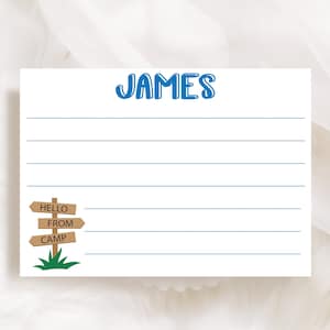 May include: A white card with blue lines and the name "JAMES" at the top.  The card has a small illustration of a wooden signpost with the words "HELLO FROM CAMP" on it.
