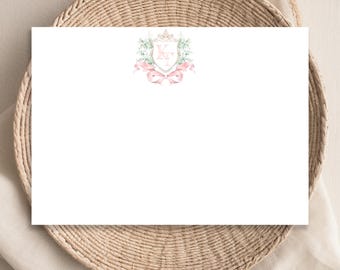 May include: A white card with a pink and green watercolor crest featuring the initials "K.T." surrounded by a crown and floral accents.