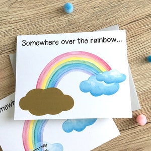 May include: A white card with the text "Somewhere over the rainbow..." printed on it. A rainbow with a gold cloud is illustrated on the card.