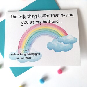 May include: A white card with a rainbow and clouds illustration. The text on the card reads "The only thing better than having you as my husband... is our rainbow baby having you as an DADDY!"