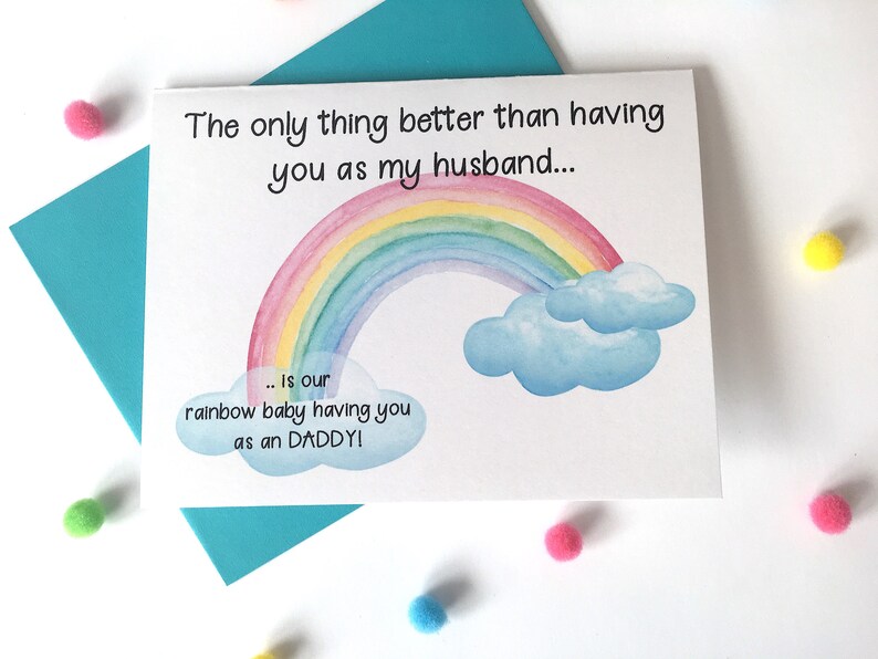 May include: A white card with a rainbow and clouds illustration. The text on the card reads "The only thing better than having you as my husband... is our rainbow baby having you as an DADDY!"
