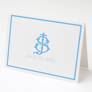 Puede incluir: Una tarjeta blanca con un borde azul claro y un monograma azul claro de las letras "JS" en una fuente decorativa. El texto "JACKLYN SMITH" está impreso debajo del monograma.