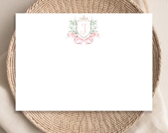 May include: A white card with a pink and green watercolor design of a crest with a crown and the letter J in the center. The crest is surrounded by a pink ribbon.