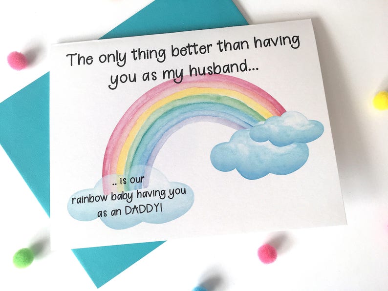 May include: A white card with a rainbow and clouds illustration. The text on the card reads "The only thing better than having you as my husband... is our rainbow baby having you as an DADDY!"