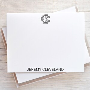 Könnte beinhalten: Weißes Briefpapier mit einem dekorativen Initial und dem Namen "JEREMY CLEVELAND" in Schwarz gedruckt. Das Briefpapier befindet sich in einer transparenten Kunststoffhülle auf einer hellen Holzoberfläche. Das Initial ist im Vintage-Stil gehalten.