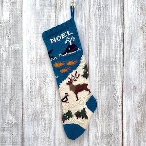 Peut inclure: Une chaussette de Noël en tricot bleu et blanc avec un motif de renne, de poissons et de baleine. La chaussette est brodée du mot "NOEL".