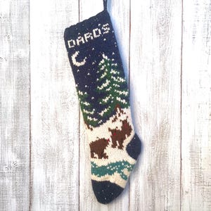 May include: A navy blue and white knitted Christmas stocking with a winter scene. The stocking features a forest, bears, and the name "DARO'S" at the top. The stocking is approximately 46 cm long.