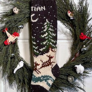 Könnte beinhalten: Ein brauner und weißer gestrickter Weihnachtsstrumpf mit einem grünen Tannenbaum, Rentieren und Schneeflocken. Der Strumpf trägt den Namen "Ryan" auf der Vorderseite.