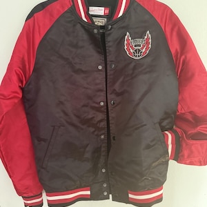 May include: A black and red satin varsity jacket featuring a Mitchell & Ness Hardwood Classics label at the neck. The chest displays a Blazers basketball logo with wings. It has a snap-button front closure and striped ribbed cuffs and hem.