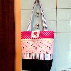 May include: A pink and white polka dot tote bag with a pink and white striped fabric panel and a black denim bottom. The bag has a pink fabric flap with a red button and a pink and white patterned fabric panel with sewing themed images. The bag has a white lace trim and a pink and white striped strap.