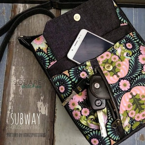 Op de afbeelding: Een zwarte crossbody tas met een bloemenprint en een ritssluiting. De tas is open en laat een telefoon en sleutels zien. De tas is gelabeld met "SUBWAY CROSSBODY BAG" en "PATTERN BY IMAZZPATTERNS".