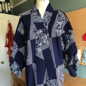 Puede incluir: Un kimono azul marino con un patrón geométrico blanco. El kimono tiene un estilo japonés tradicional con mangas anchas y cuello en V.