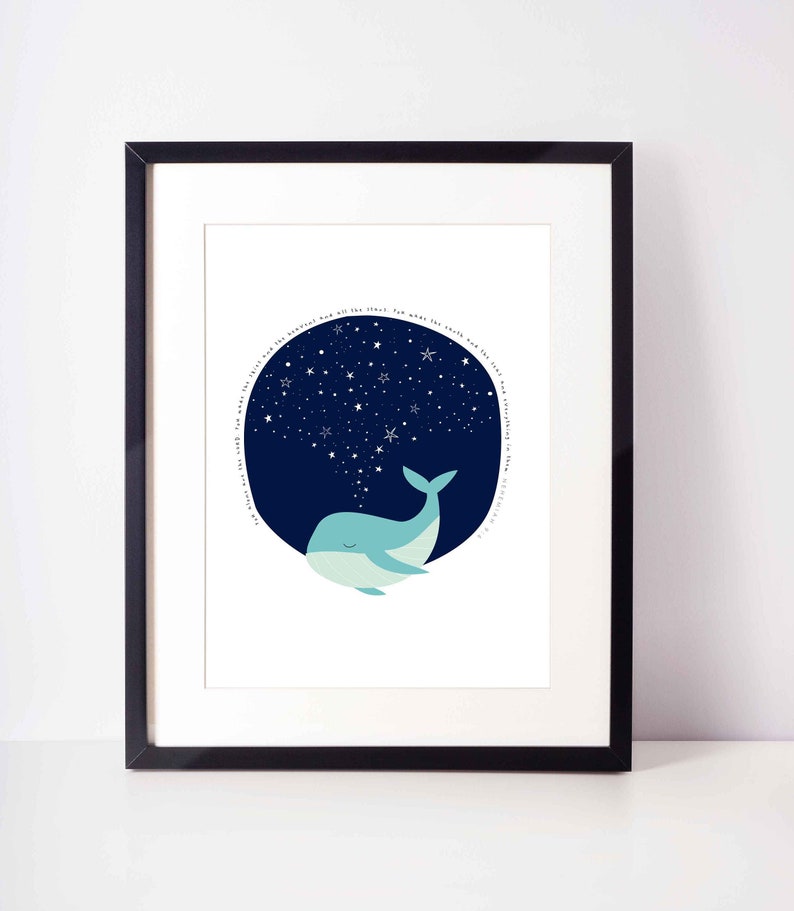 May include: A framed art print featuring a whimsical illustration of a light blue whale with closed eyes, beneath a dark blue circle filled with white stars. The print includes a circular text in white.
