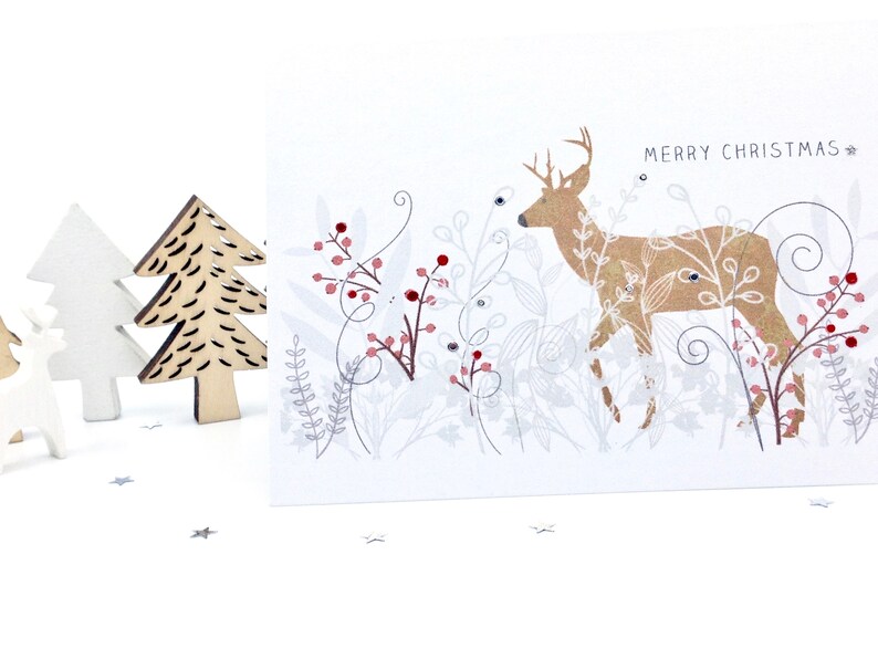 Op de afbeelding: Een witte kerstkaart met een gouden hert-illustratie en de tekst "Merry Christmas" in zwart. Het hert is omringd door zilveren en rode bessen en bladeren.