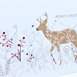 Op de afbeelding: Een witte kerstkaart met een gouden hinde-illustratie en de tekst "Merry Christmas". De hinde is omringd door rode bessen en wit blad.