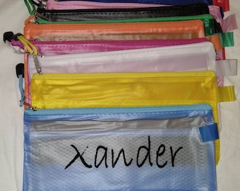 May include: A stack of ten colorful mesh zippered pouches with a blue pouch at the bottom that has the name "Xander" written on it.