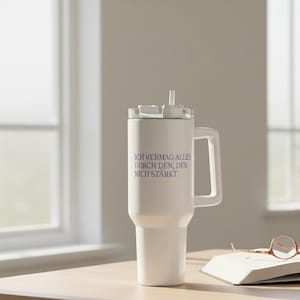 Könnte beinhalten: Ein weißer isolierter Becher mit Griff und transparentem Deckel. Der Becher hat einen Strohhalm und den Text "ICH VERMAG ALLES DURCH DEN, DER MICH STÄRKT" in Lila. Der Becher steht auf einer Holzoberfläche.
