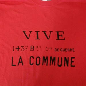 May include: Red t-shirt with black text that reads "VIVE 143e Bon Cies De Guerre LA COMMUNE".