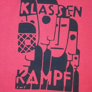 May include: Black and white graphic print on a red t-shirt. The print features three stylized faces and the text "KLASSENKAMPF".