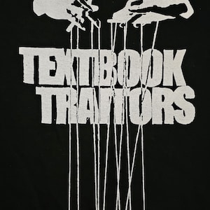 May include: Black and white graphic design of two hands manipulating strings that are attached to the text "TEXTBOOK TRAITORS".
