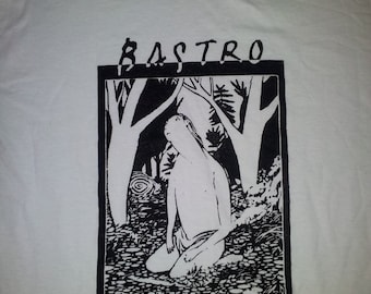 May include: White crew neck t-shirt with a black and white graphic. The graphic features the word "BASTRO" above a black rectangle containing a forest scene and a figure kneeling in the center.