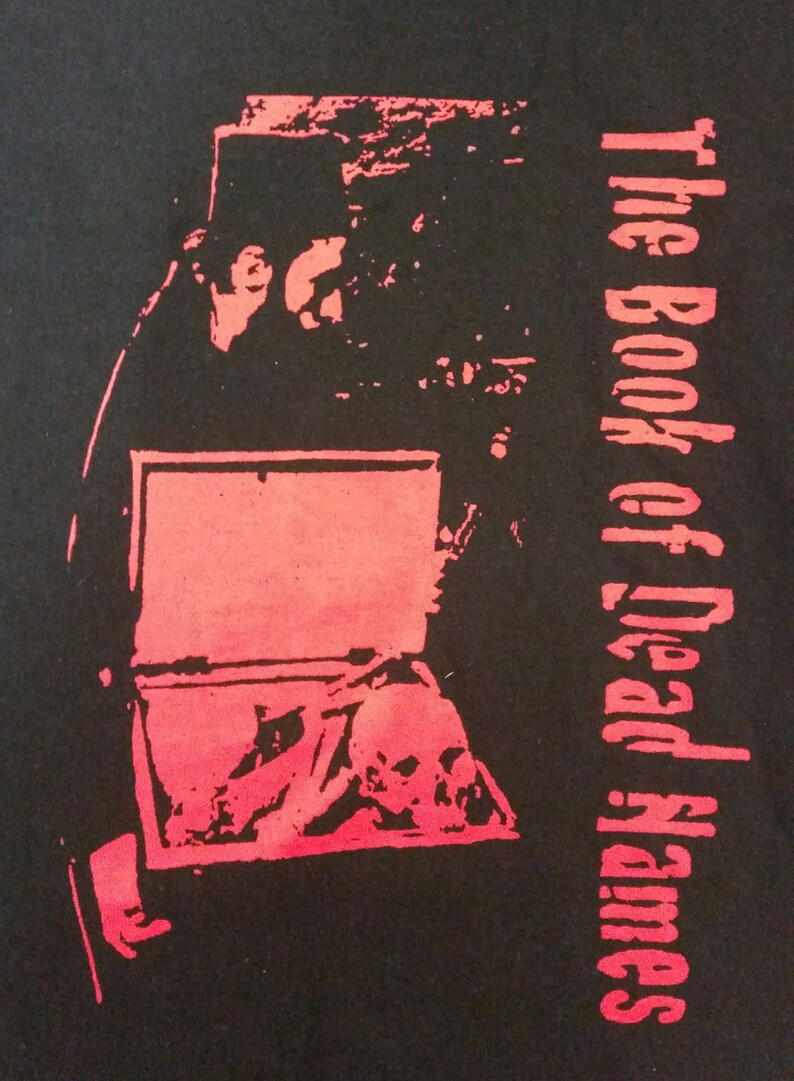 May include: A black t-shirt with a red graphic print of a coffin with a skull inside. The text "The Book of Dead Names" is printed vertically on the right side of the image.