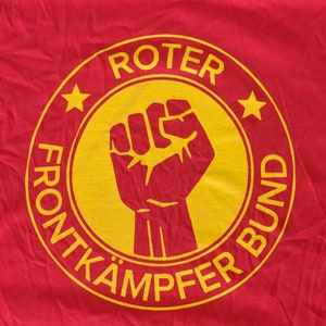 May include: A red t-shirt with a yellow circle logo. The logo features a raised fist and the text "ROTER FRONTKÄMPFER BUND".