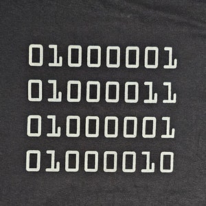 Puede incluir: Una camiseta negra con el código binario "010000001" repetido cuatro veces en blanco.