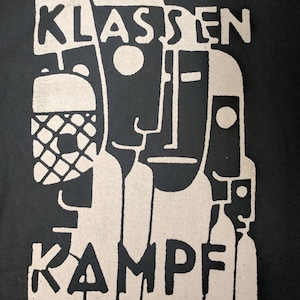 May include: Black and white graphic print with the text "KLASSEN KAMPF" in a bold, stylized font. The design features abstract figures with geometric shapes.