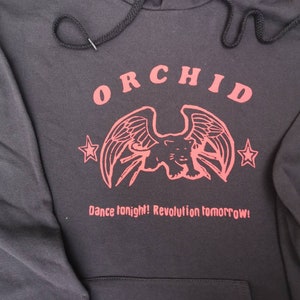 May include: Black hooded sweatshirt with a red graphic print of a winged panther with the word "ORCHID" above it and the text "Dance tonight! Revolution tomorrow!" below it.