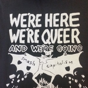 Könnte beinhalten: Schwarzer Kapuzenpullover mit weißem Text, der "We're here, we're queer, and we're going shoplifting" lautet. Ein Cartoon-Monster mit Flügeln ist dargestellt, wie es den Kapitalismus zerschlägt.