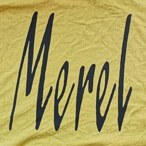 Puede incluir: Un fondo de tela amarillo con la palabra "Merel" escrita en cursiva negra.