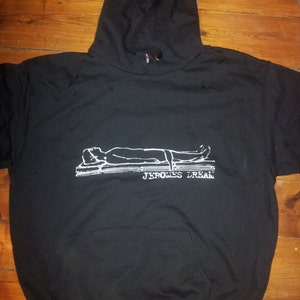 Könnte beinhalten: Schwarzer Kapuzenpullover mit einem weißen Grafikdruck einer Person, die auf einem Bett liegt, mit dem Text "JEROMES DREAM" darunter.